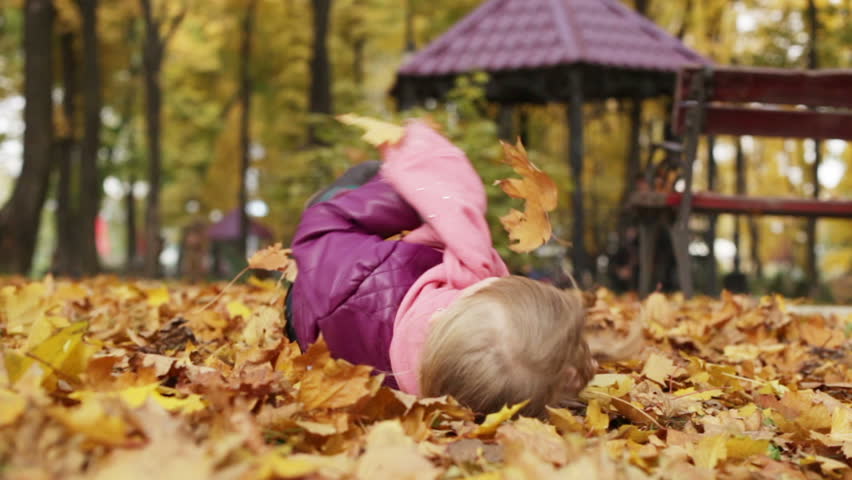 Little girl tumbles in the yellow autumn leaves. Autumn leaf fall. The child