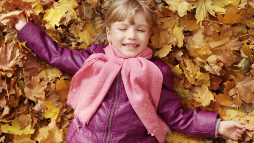 Little girl lying in yellow leaves. Autumn leaf fall. The child lying on the