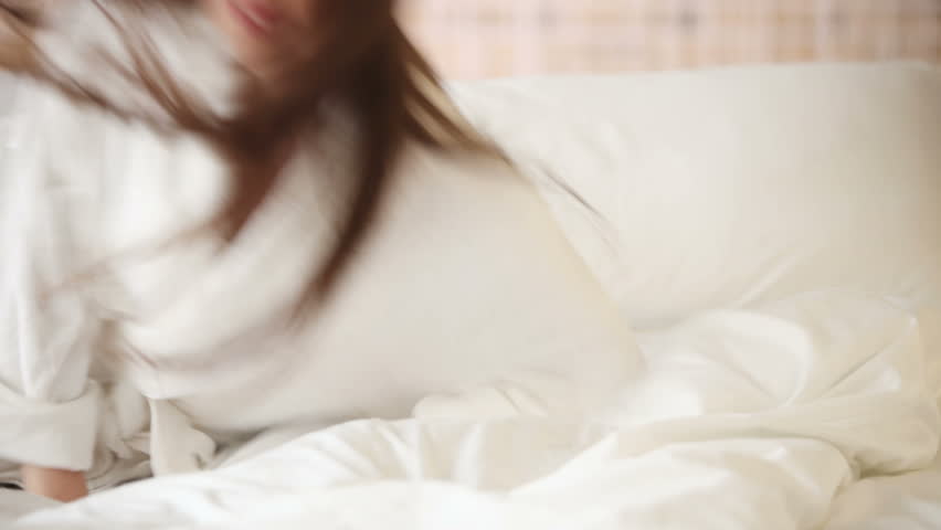 Cheerful girl falling on bed laughing and smiling at camera. Panning camera