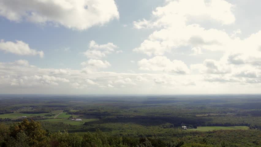 Luminous clouds flowing over a broad expanse of countryside dotted with farms and forest. Early fall colors are beginning to show. View from Rib Mountain, Wisconsin, midwest USA.