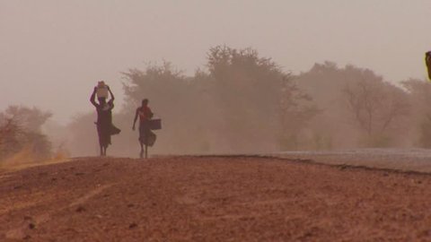 Women walk carrying goods on their heads through the Sahara desert in mali.