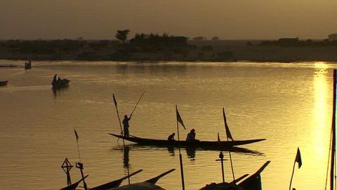 Boats are rowed on the Niger River in beautiful golden light in Mali, Africa.