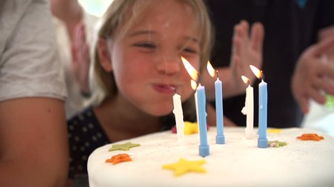 Little girl blows out candles on birthday cake at party, slow motion sequence