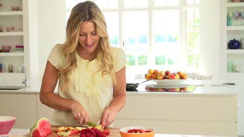 Woman cutting summer fruits on chopping board to make fruit salad