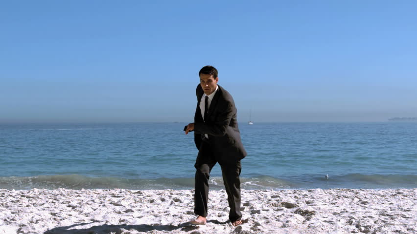 Handsome businessman jumping and kicking on the beach in slow motion