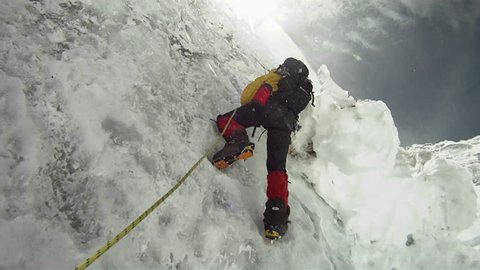 Climber on icy wall with wind and snow blowing