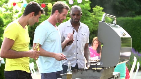 Three men cooking on barbecue and toasting beer bottles in backyard