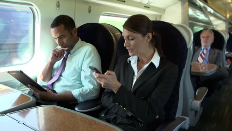 Businessman using digital tablet while female colleague talks on mobile phone on commuter train Stock Video