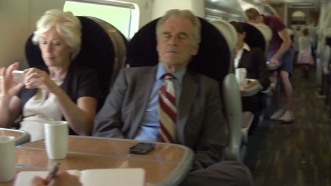 Camera pans from businessman using digital tablet to fellow passengers in next seat using mobile phones and sleeping