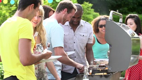 Men serving burgers, kabobs, and corn from backyard barbecue for summertime dinner party