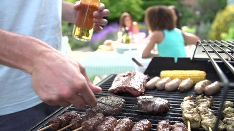 Close up of man food grilling on barbecue while women sit at backyard table and relax