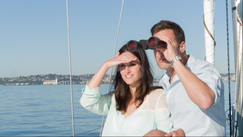 Young couple have fun looking through binoculars while on a sail boat in