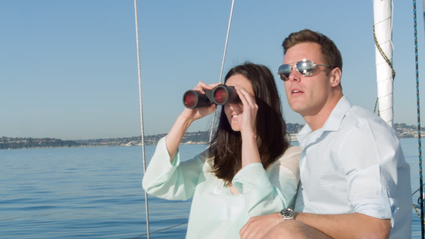 Young couple have fun looking through binoculars while on a sail boat in