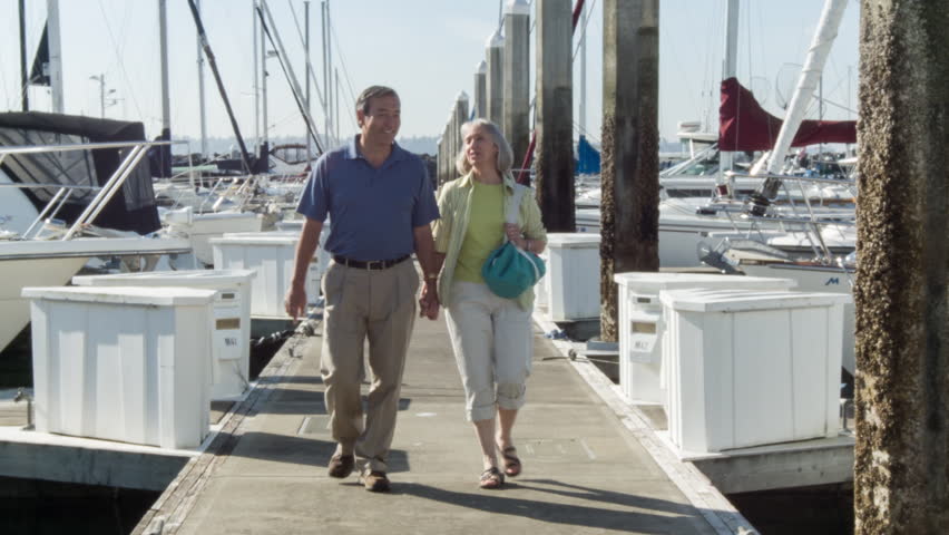 Mature couple talking and having fun as they walk past sail boats in Seattle,