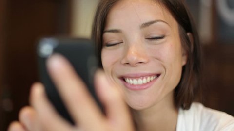Smartphone girl using app on phone drinking coffee smiling in cafe. Beautiful multicultural young casual female professional on mobile phone. Mixed race Asian Caucasian model.