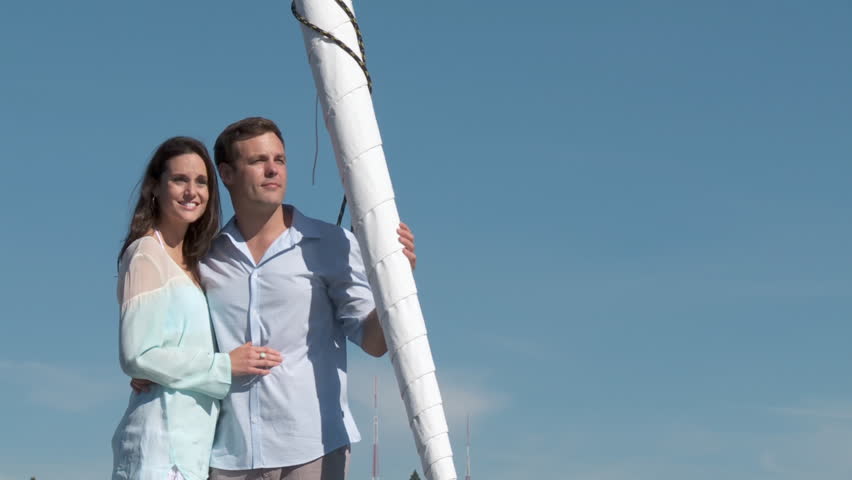 Young couple stand at the front of a boat as they set sail.  Neutral background