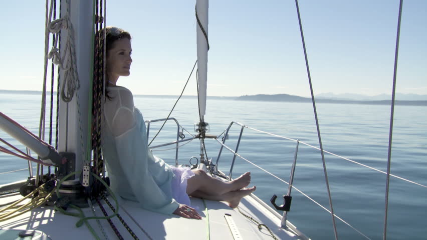 Young woman sitting on the deck of a boat, sailing towards distant mountains. 