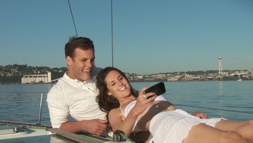 Attractive couple relaxes, taking photos and using a smartphone on a sailboat