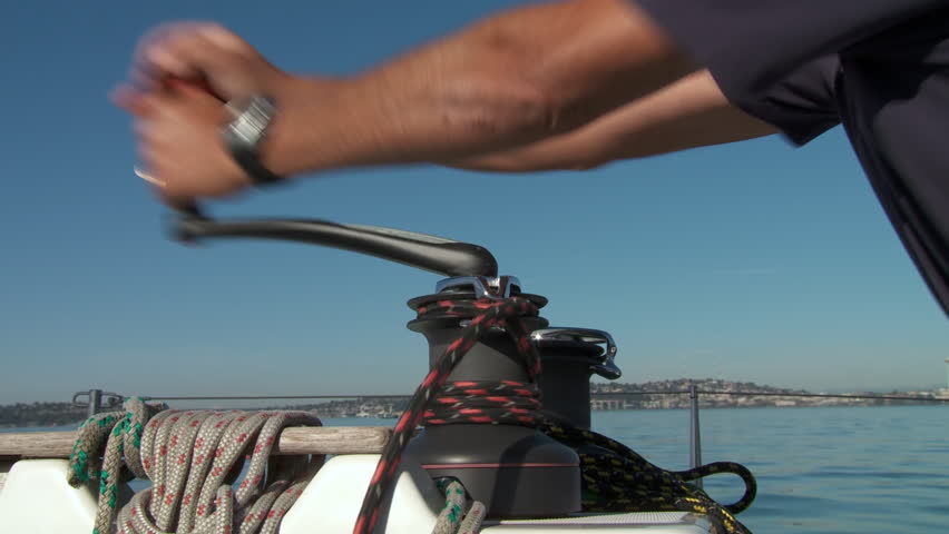 Close up of hands winching a rope (sheet) on a sail boat as it travels on the