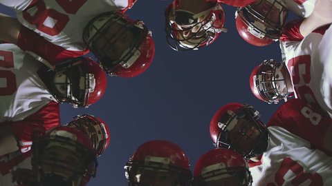 The camera looks up into a huddle full of football players talking before a play