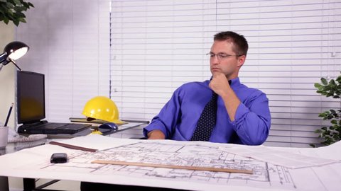 A young architect, builder, or designer in his office going over a set of house plans he is working on.  Jib used for footage.
