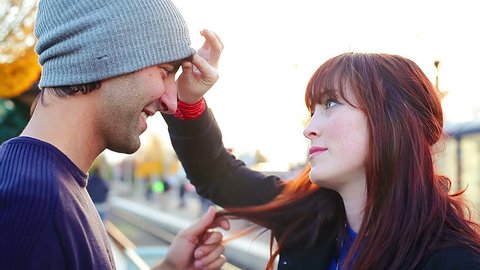 A young couple kiss and flirt while they wait on a train platform for the next arrival, close up