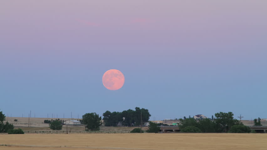 The July Supermoon Full Moon rises over Interstate 25 Highway at dusk in rural