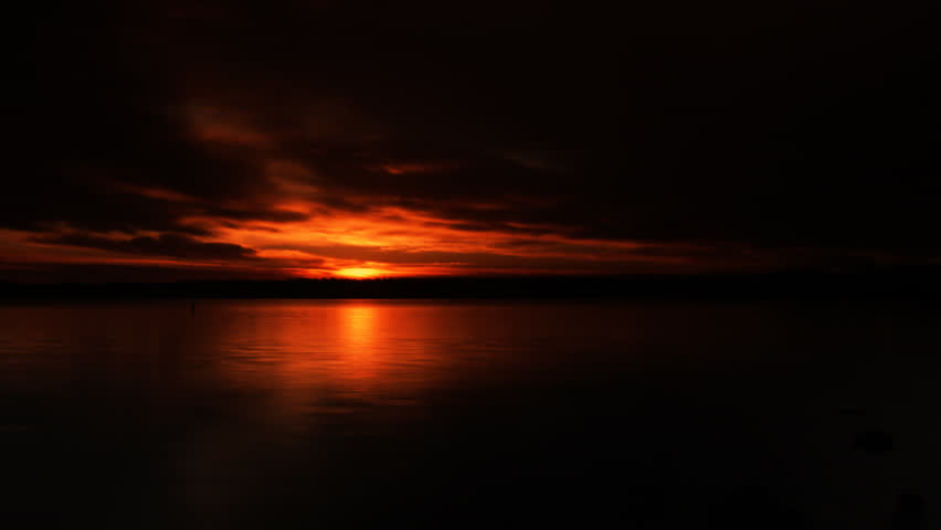 Glowing red sunrise over lake, with low clouds. HD 1080p time lapse