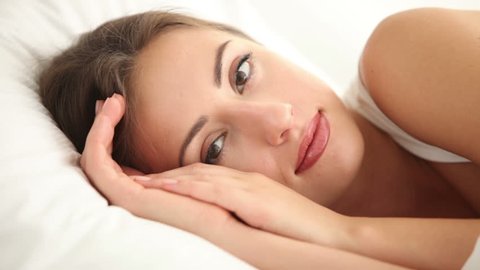 Beautiful girl lying in bed looking at camera closing her eyes and falling asleep