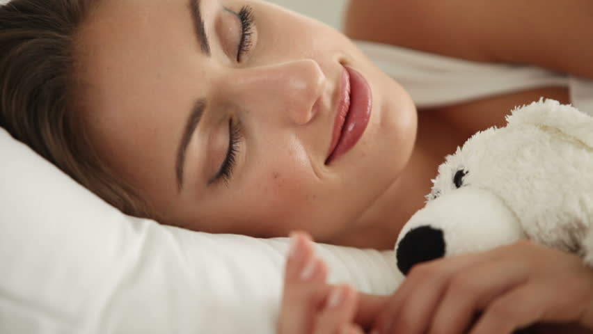 Attractive girl sleeping in bed and hugging teddy bear. Panning camera