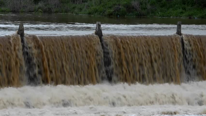 Flood waters rush over the side of a dam.