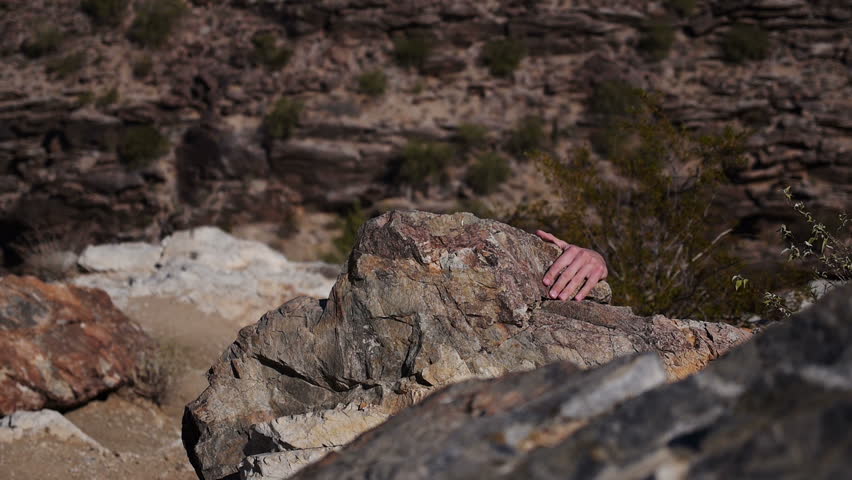 A young man pretends to climb up a cliff in the desert.