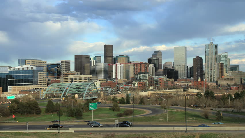 Denver, Colorado skyline on a sunny evening, with highway traffic in foreground.
