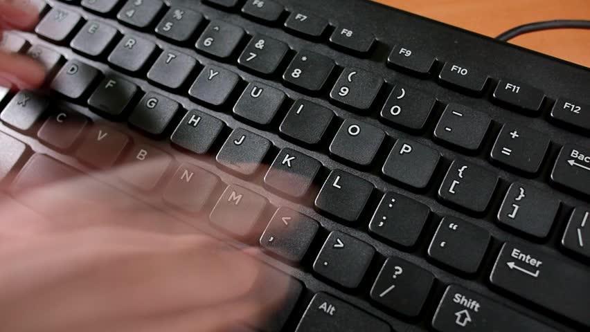 Man typing on a PC computer keyboard. A low shutter speed gives the motion blur