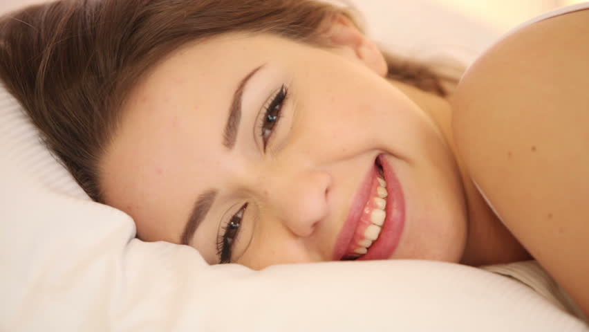 Beautiful girl sleeping in bed waking up and smiling at camera. Panning camera