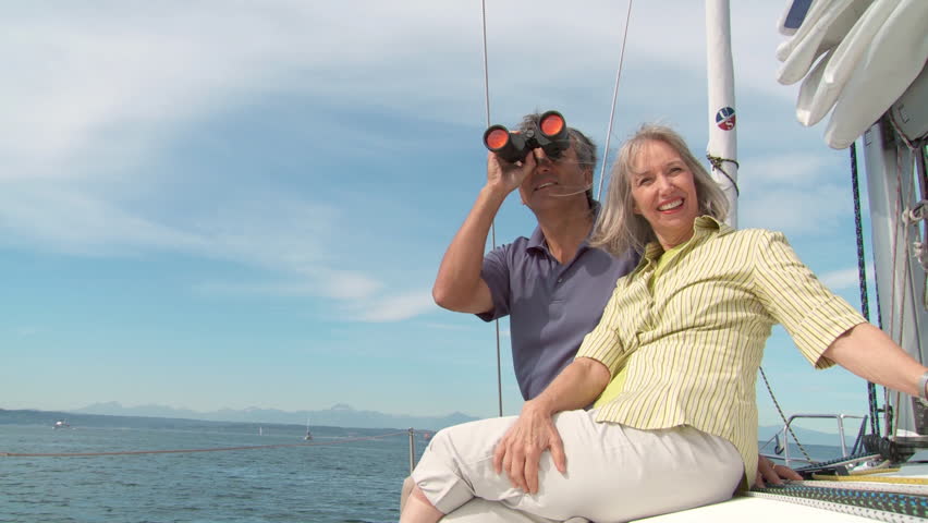 Mature couple looking through binoculars while sitting on the deck of a boat,