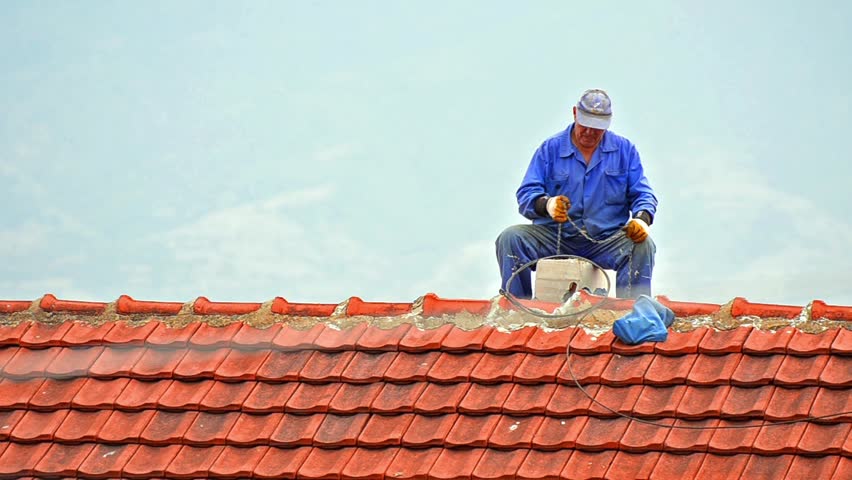 Chimney sweep cleaning a chimney sitting balanced on the apex of a house roof