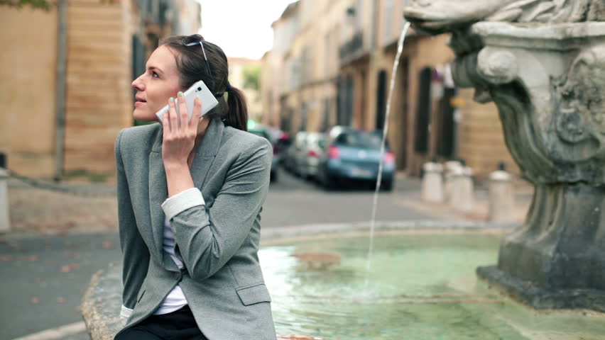 Beautiful woman talking on cellphone by the fountain in city
