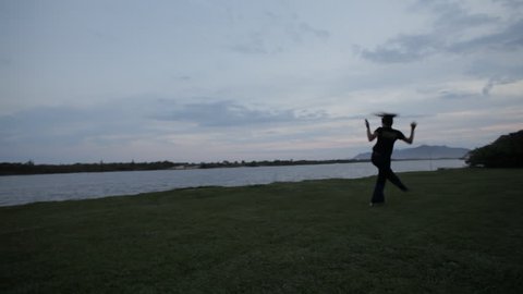 woman playing capoeira next to the river at sunset
