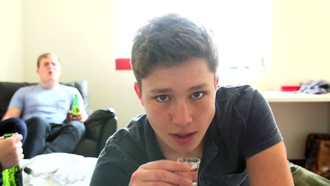 Teenage boy takes a shot of clear liquor and grimaces in slow motion