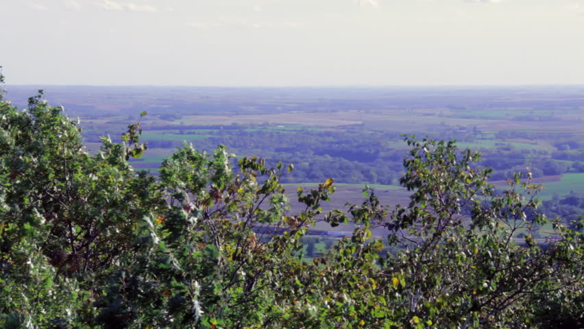 An expansive view of Wisconsin countryside in the Fall. Shot from the Blue Mounds State Park hill, clouds soar over treetops bright with fall colors, green fields, farmhouses and rural homesteads.