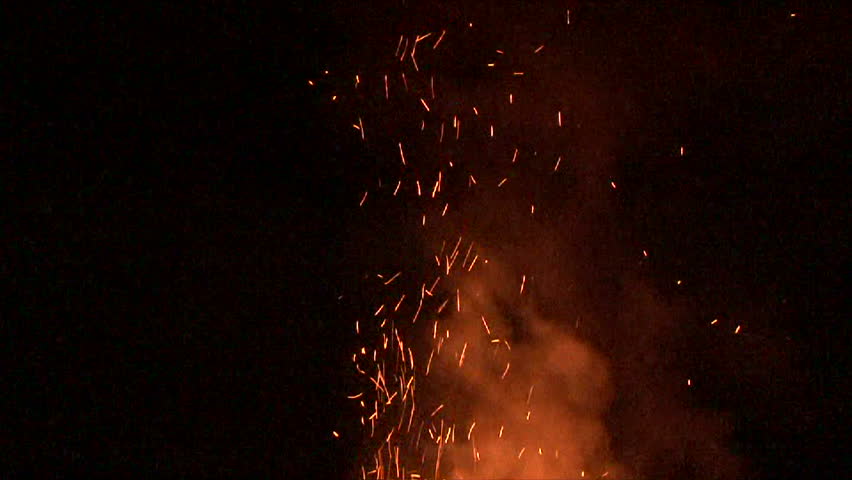 Large fire burning at night with smoke and sparks rising.