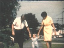 1960s, 8mm vintage, archival film home movies of mom and dad teaching toddler son to walk on neighborhood sidewalk, Seattle, Washington.