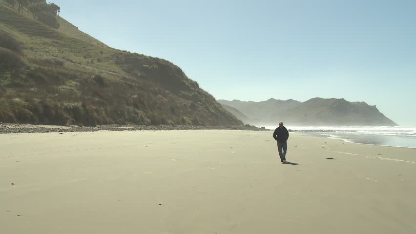 A middle aged man walking along a deserted beach