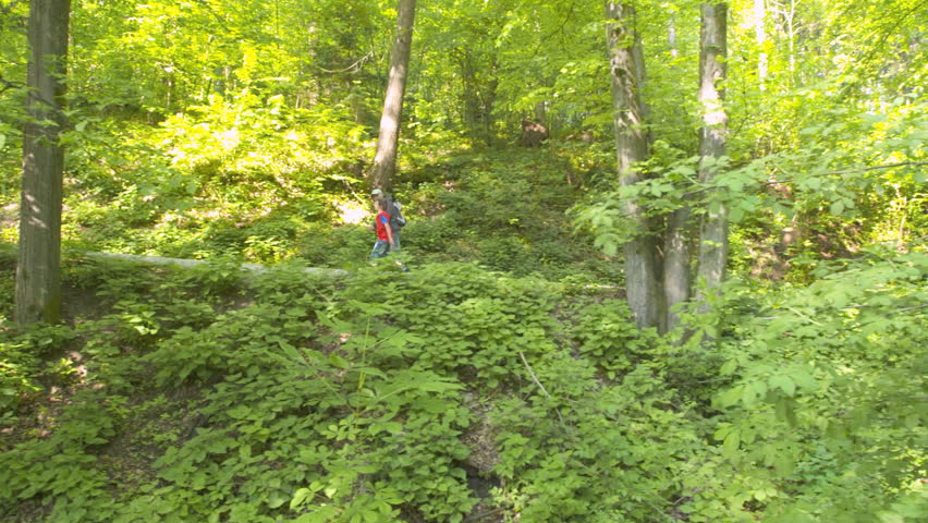 Dolly Shot Of Grandfather And Grandson Hiking Through Green Forrest 