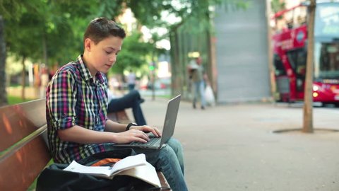 Young teenager writing, doing homework on laptop in the city
