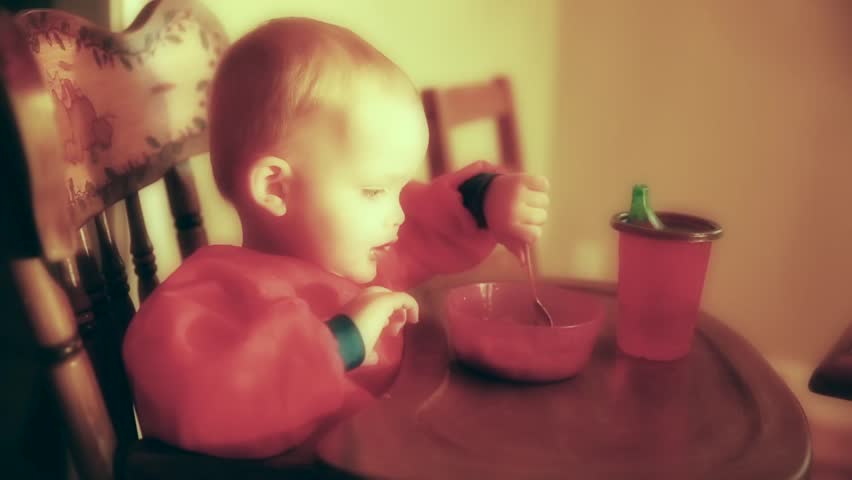 A little baby boy eating stew in his high chair in the kitchen at his home