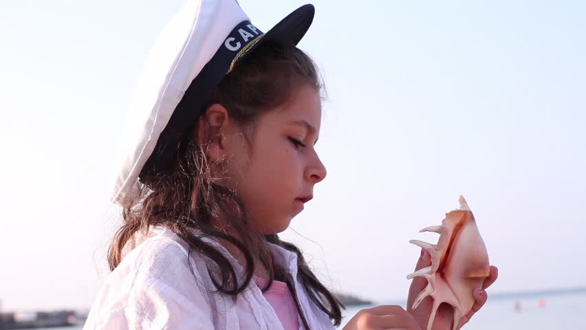 Young girl standing at beach holding shell up to ear