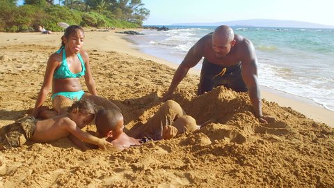 A father and his daughters try to bury a boy in the sand