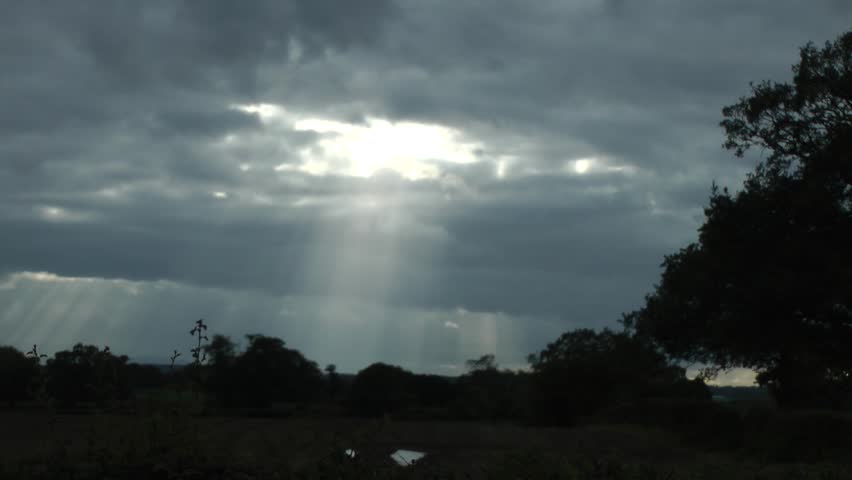 Sunbeams through clouds with silhouetted landscape of trees 